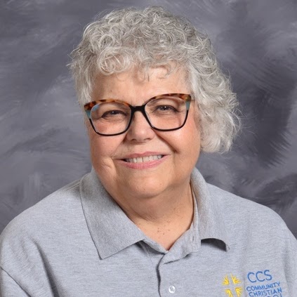 Older woman with curly gray hair and glasses smiles warmly