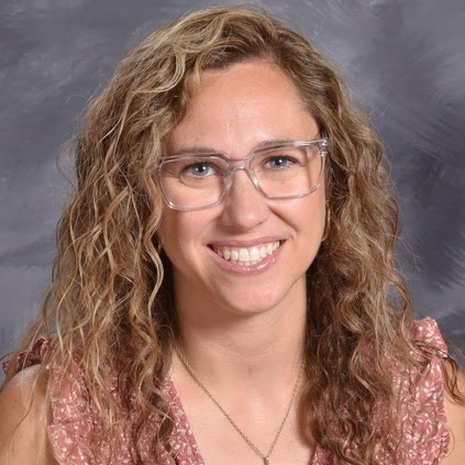 Smiling woman with curly hair and glasses, wearing a pink top