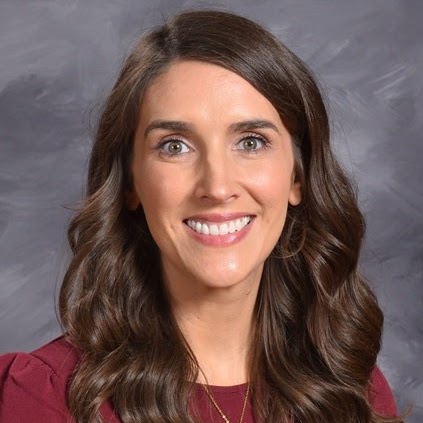 Smiling woman with long, wavy brown hair and a light brown top