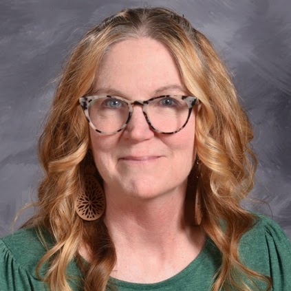 Smiling woman with wavy, shoulder-length hair, wearing glasses and large earrings