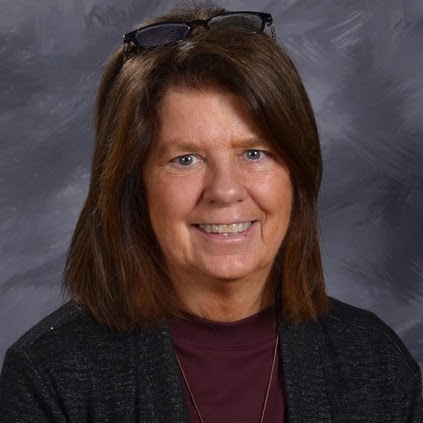 A smiling woman with brown hair, wearing a black cardigan over a maroon top