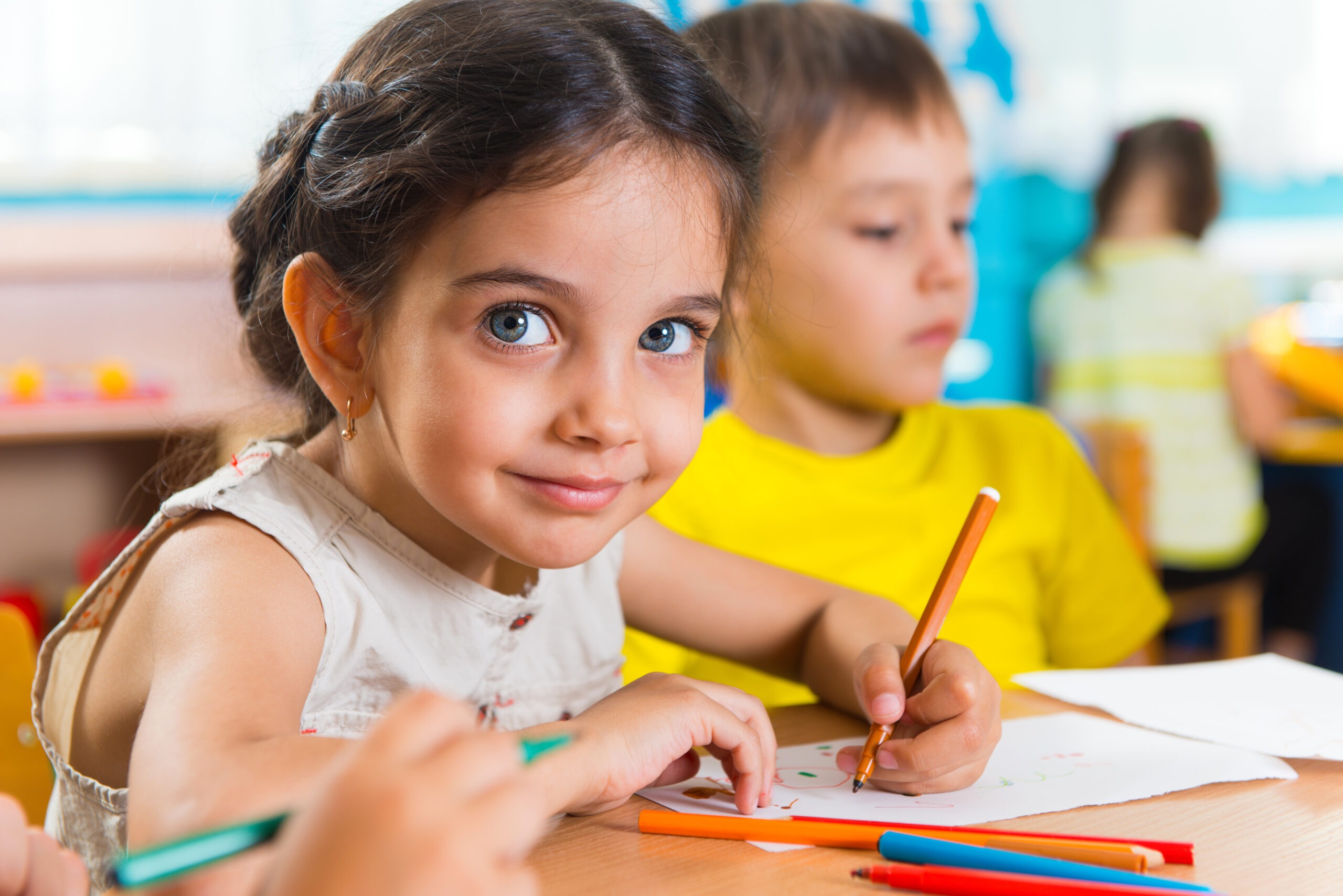 A young girl with braided hair smiles while coloring with crayons at a table