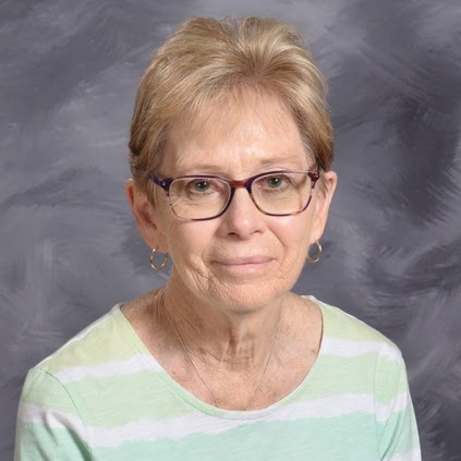 A woman with short blonde hair and glasses smiles gently
