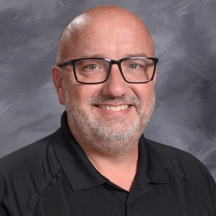Smiling man with glasses and a beard, wearing a black polo shirt